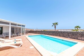 A pool area with lounge chairs, a covered seating area, and a stone wall. - Villa Papagayo Faro by Villa Plus (Playa Blanca)