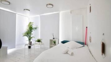 A modern bedroom with a large bed, a potted plant, and a small side table.