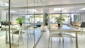Un salón de conferencias moderno con paredes de vidrio, mobiliario blanco y plantas en macetas.