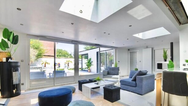 Una sala de estar moderna con un amplio ventanal que da a un espacio exterior, un sofá, otomanas y una mesa de centro.