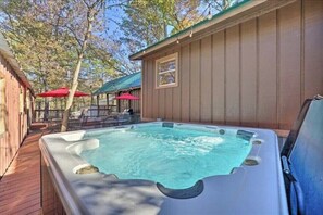 A hot tub with a wooden deck, surrounded by a wooden cabin with a green roof and red umbrellas. - Hunting Daze- 2 Large Deck with Hot Tub and Fire Pit in heart of Hochatown! (Broken Bow)
