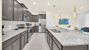A modern kitchen with dark cabinets, granite countertops, stainless steel appliances, and pendant lighting. - Modern 5BR Home w/ Pool at Windsor Island (Davenport)