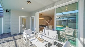 A modern outdoor patio with white furniture, a glass-enclosed dining area, and a view of the pool. - Modern 5BR Home w/ Pool at Windsor Island (Davenport)