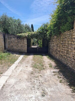 A stone wall with a metal gate, a dirt path, and greenery. - Guest rooms adjoining the main house with a separate entrance (Bédoin)