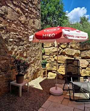 A stone wall, a potted plant, a folding chair, and a MIKO branded umbrella.