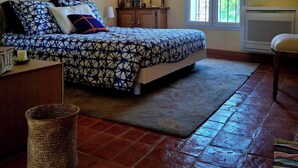 Quarto com cama, mesa de cabeceira, luminária, janela e radiador.