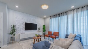 Ein modernes Wohnzimmer mit einem an einer strukturierten Wand montierten Flachbildfernseher, einem Sofa, zwei Sesseln, einem Couchtisch und einem Blumentopf.