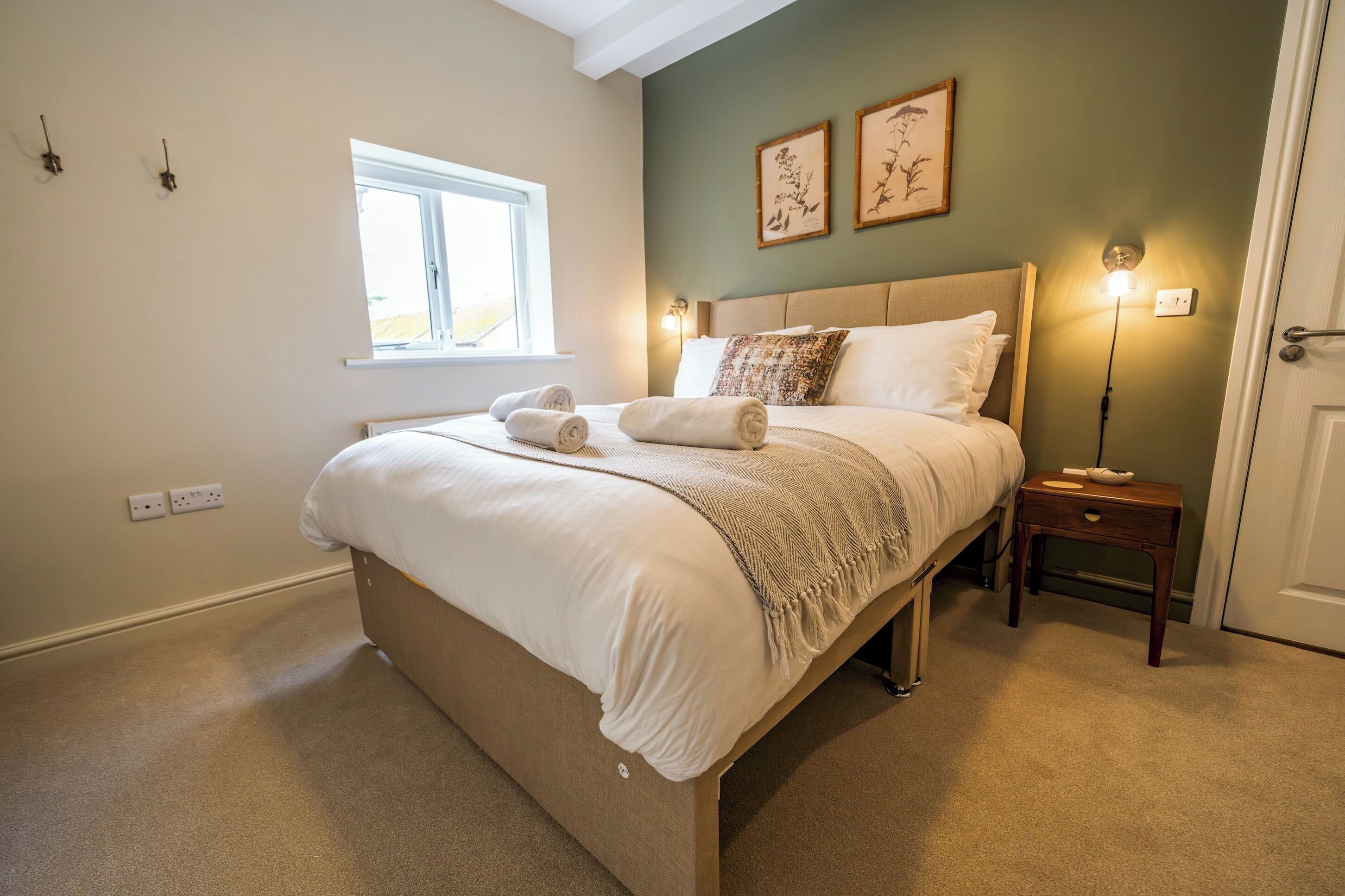 A bedroom with a bed, bedside table, wall art, and a window.