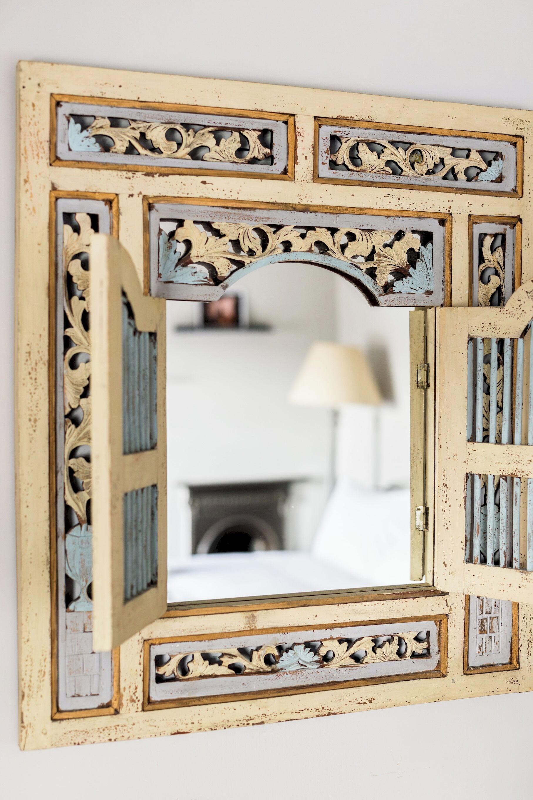 A mirror with ornate, distressed frame and a view of a room with a lamp.