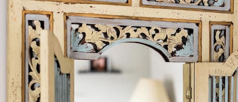 A mirror with ornate, distressed frame and a view of a room with a lamp.