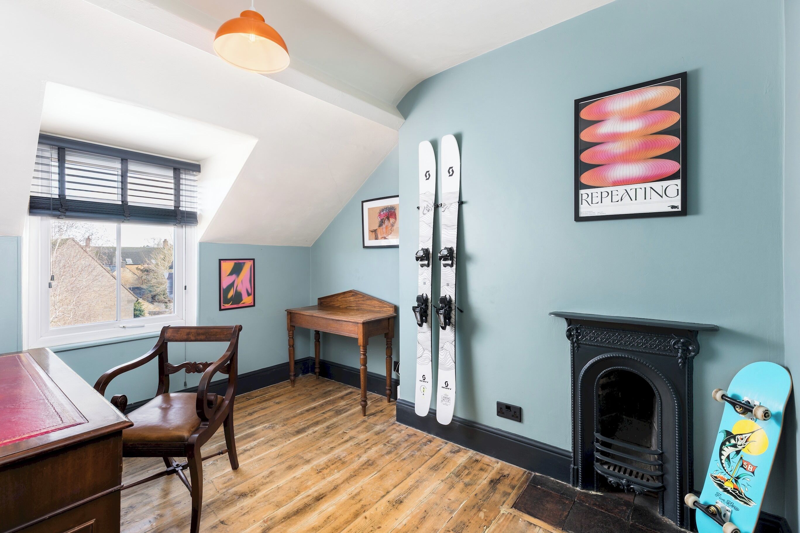 A room with a wooden floor, a fireplace, a table, a chair, and skis mounted on the wall.