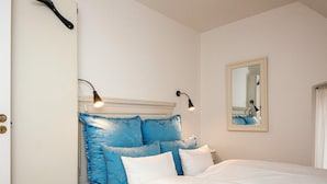 A neatly made bed with white and blue bedding, a headboard with decorative blue panels, two bedside lamps, and a mirror on the wall. - 4 Star Holiday Home in Skanderborg (Skanderborg)
