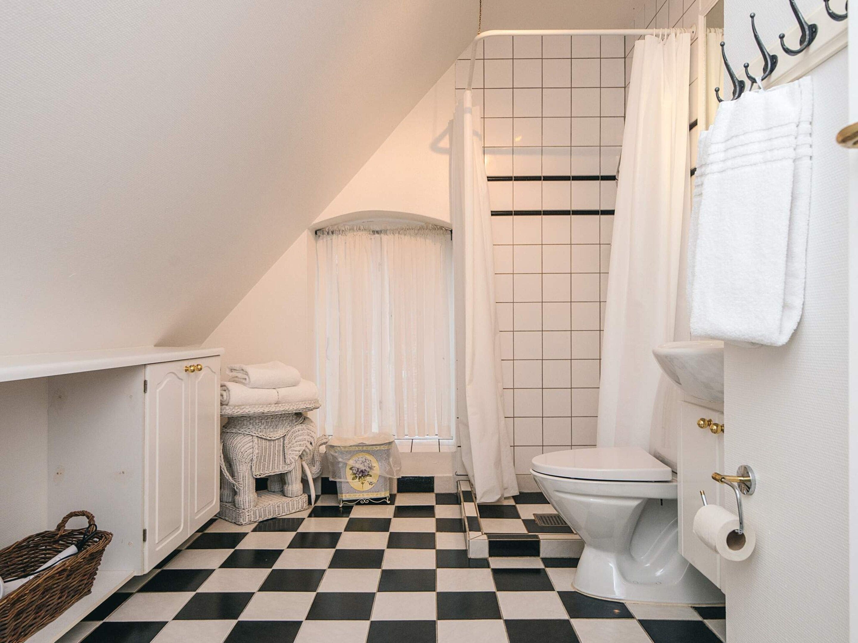 Une salle de bain avec un carrelage à motifs géométriques, des toilettes blanches, un rideau de douche et un porte-serviettes.