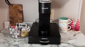 A kitchen with a Keurig coffee maker on a marble countertop, a mug with a message, and a glass container with coffee pods. - 3-bedroom house ~ Pro Cleaned - Work & Family Friendly (Racine)