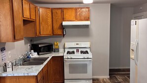 A kitchen with wooden cabinets, a white stove, a microwave, and a refrigerator. - 3-bedroom house ~ Pro Cleaned - Work & Family Friendly (Racine)
