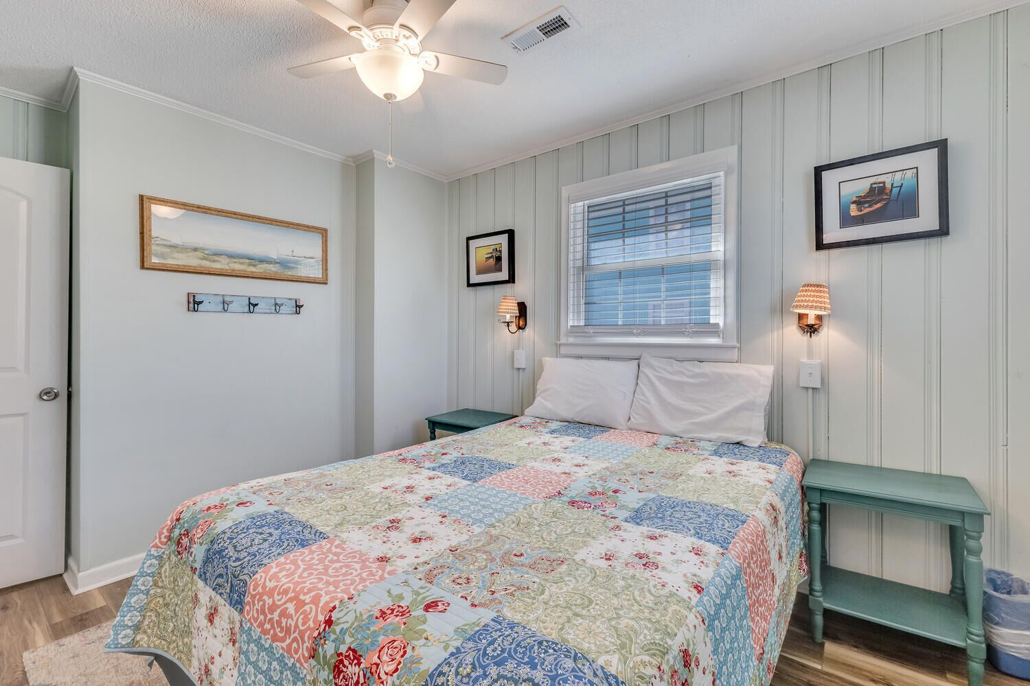 A bedroom with a bed, a ceiling fan, a window with blinds, and wall-mounted lamps.