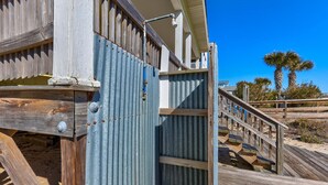 A wooden beach house with a metal gate, a wooden staircase, and a clear blue sky. - Helen and AJ: Oceanfront 6-Bedroom Duplex Retreat | Two Units, One Incredible St (Carolina Beach)