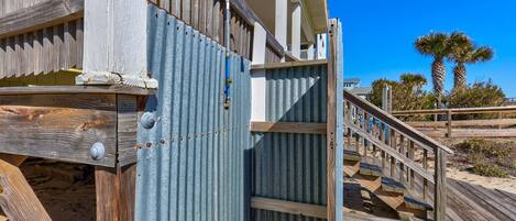 Una casa de playa de madera con un portón metálico, una escalera de madera y un cielo azul despejado.