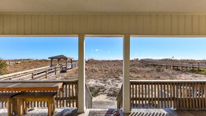 A beach view from a covered deck with wooden railings and a wooden bench. - Helen and AJ: Oceanfront 6-Bedroom Duplex Retreat | Two Units, One Incredible St (Carolina Beach)