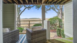 A covered porch with wicker furniture and a view of a rural landscape. - Seabrook Exclusives | 1722 Shelter Cove (Seabrook Island)