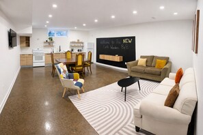A modern living room with a sofa, armchair, and coffee table. A chalkboard sign reads "Welcome to The NEW Earth Wonders B&B." - West Toronto Luxury B&B Humber River Suite - Steps to UP Express - Airport-Union (Toronto)