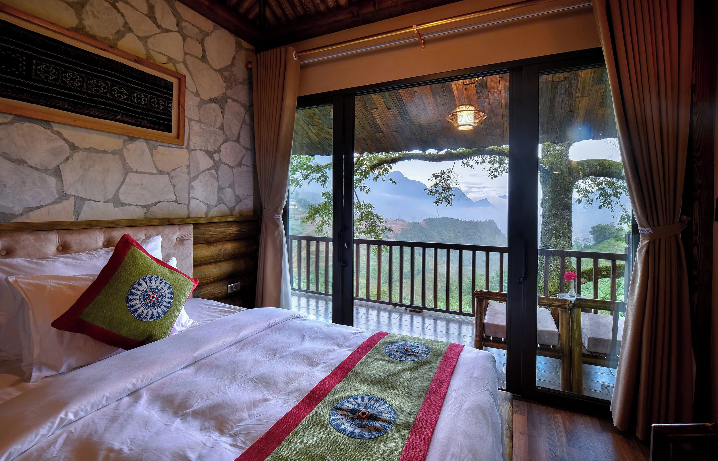 Habitación de hotel con cama, vistas a las montañas y un balcón con mesa y sillas.