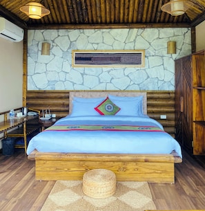 A wooden-framed bed with a blue bedspread and decorative pillows, a stone wall with a framed sign, and a wooden ceiling with hanging lights. - Chapa Ecolodge (Sa Pa)