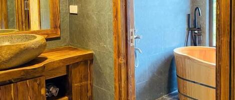 Un baño con tocador de madera, un lavabo grande tipo cuenco, una bañera independiente y una ducha con cabezal de ducha de mano.