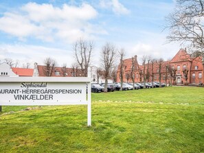 A sign for 'Sophiendal Restaurant-Herregårdspension Vinkælder' with a parking lot and a red brick building in the background. - 4 Star Holiday Home in Skanderborg (Skanderborg)