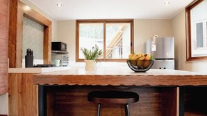 A kitchen with a wooden island, bar stools, a refrigerator, and a window with a view of a deck.