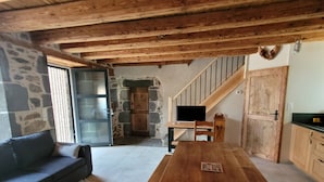 Un interno rustico con un tavolo da pranzo in legno, pareti in pietra e una scala che conduce a un piano superiore.