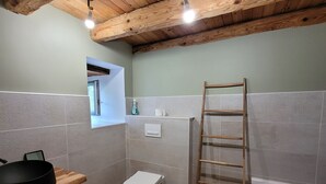 Un bagno con soffitto in legno, una vasca da bagno, un water, un lavandino e una piccola finestra.
