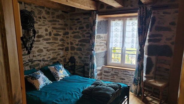 Una camera da letto con una parete in pietra, un letto con lenzuola color acquamarina, una finestra con tende e un pavimento in legno.