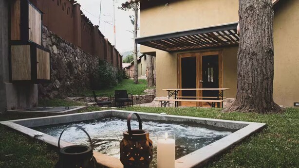 A small outdoor hot tub area with a stone wall, a wooden table, and two lanterns. - Killay A4 - Villa de lujo de 2d (Cusco)