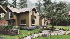 A two-story house with a stone foundation, a tiled roof, and a landscaped garden with a variety of plants and a stone pathway. - Killay A4 - Villa de lujo de 2d (Cusco)