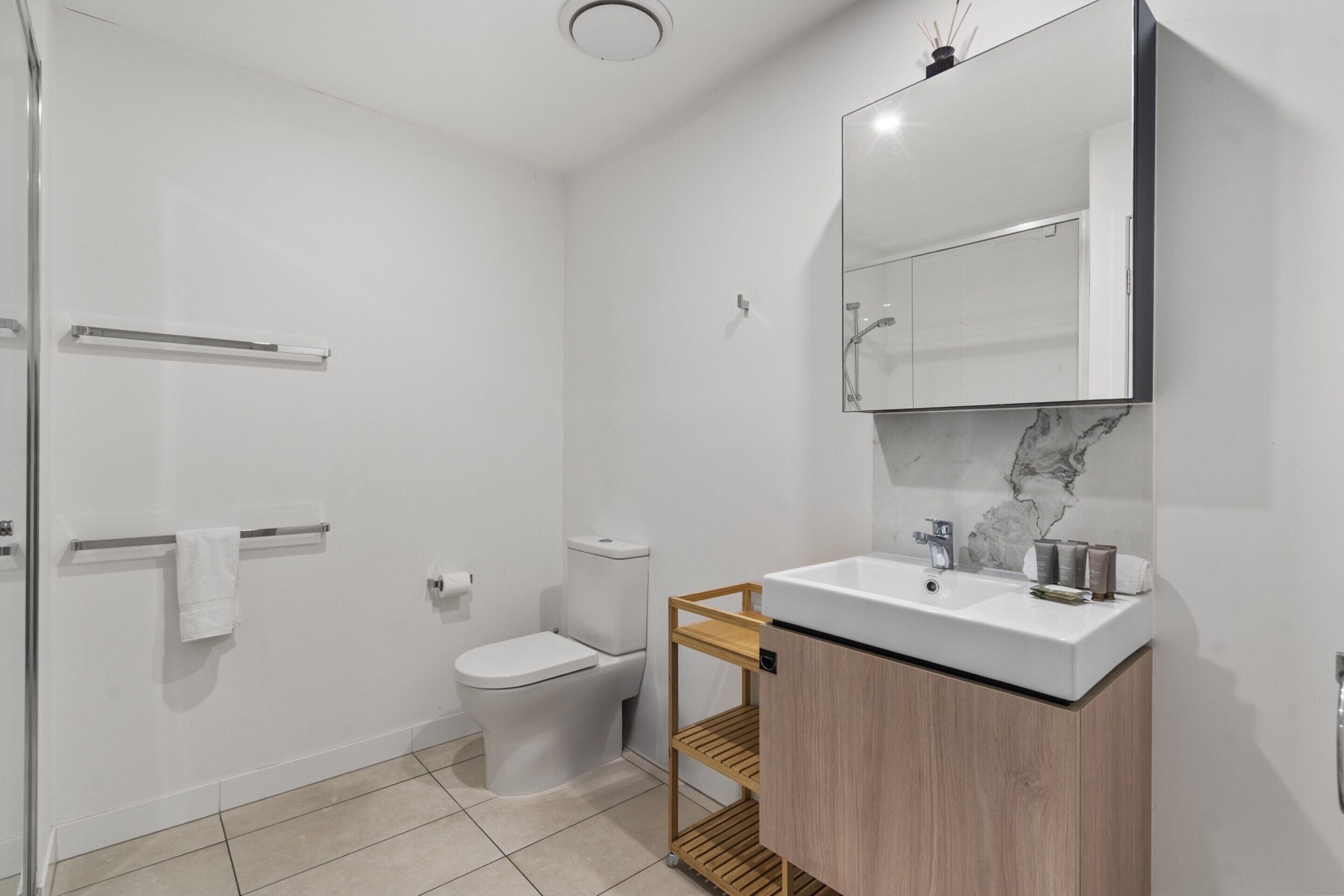 Un bany modern amb un espai de banyera de vidre, un vàter, un lavabo amb respatller de marbre i un moble de tocador de fusta.