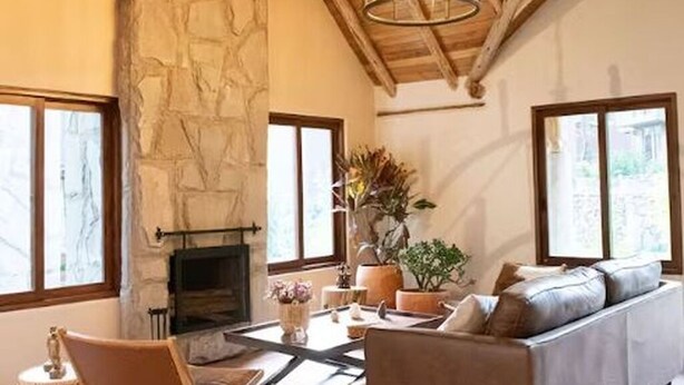 A cozy living room with a stone wall, a fireplace, a sofa, and a chandelier. - Killay B3 - Casita de 3 dorm en el Valle Sagrado! (Cusco)