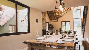 A dining area with a wooden table set for a meal, large windows, and a hanging light fixture. - Killay B3 - Casita de 3 dorm en el Valle Sagrado! (Cusco)