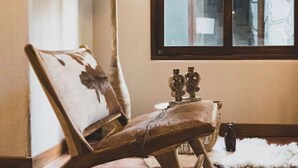 A wooden chair with a floral cushion, a small table with decorative items, and a window with a view of a building. - Killay B3 - Casita de 3 dorm en el Valle Sagrado! (Cusco)