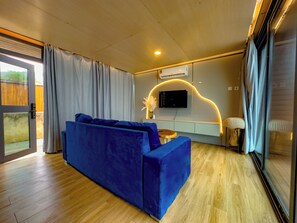 A modern living room with a blue sofa, a wooden coffee table, and a TV mounted on the wall. - Selah Beach Cabins (Kokrobite)