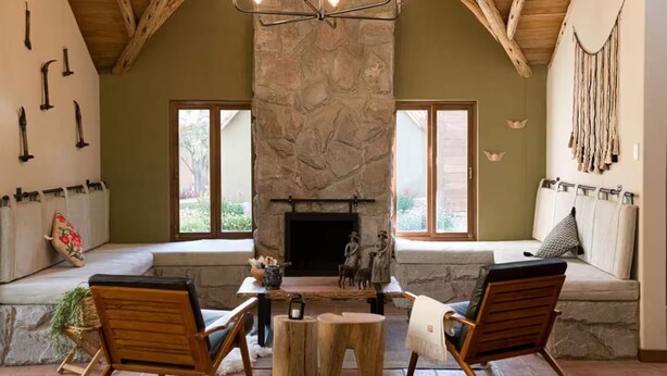 Un cuarto acogedor con chimenea de piedra, vigas de madera y una zona de estar con bancos.
