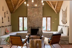 Un cuarto acogedor con chimenea de piedra, vigas de madera y una zona de estar con bancos.