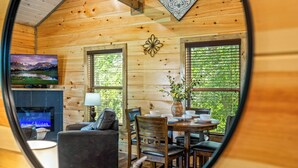 A cozy wooden cabin interior with a fireplace, a television, and a dining area with a table and chairs. - Brand New “Easy Cabin on Osprey way" (Pigeon Forge)