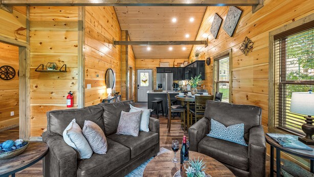 A cozy log cabin interior with two sofas, a coffee table, and a dining area. - Brand New “Easy Cabin on Osprey way" (Pigeon Forge)