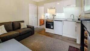 A compact living space with a kitchenette, a sofa, and a dining area. - Ground Floor Apartment Beverley House (Cromer)