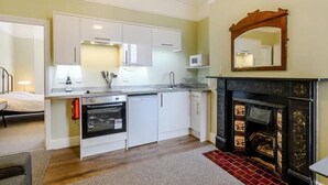 A compact kitchen with white cabinets, a microwave, a built-in oven, and a fireplace. - Ground Floor Apartment Beverley House (Cromer)