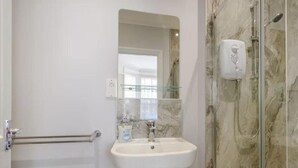 A bathroom with a white sink, a glass shower enclosure, and a marble wall. - Ground Floor Apartment Beverley House (Cromer)