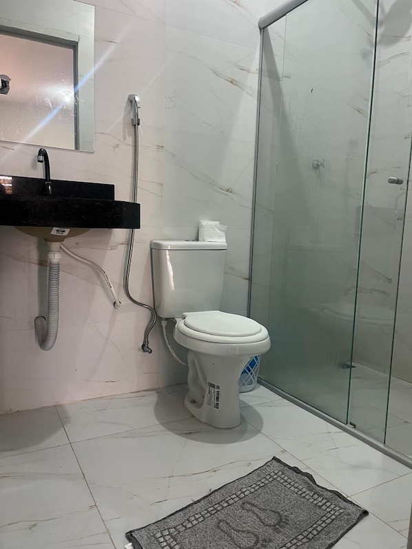 Une salle de bain comprenant des toilettes, un lavabo, une douche et une porte en verre.