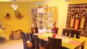 A dining area with a table set for four, surrounded by chairs. A bookshelf filled with various items is to the left, and a wall display of hats is to the right.
