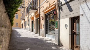 Una calle estrecha flanqueada por edificios, con balcones, una reja de metal y un muro de azulejos.